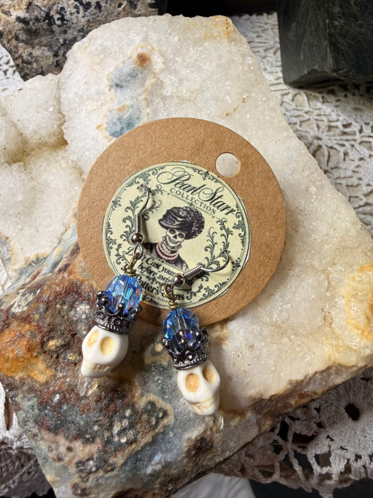Pearl Starr skull earrings with blue faceted beads, gunmetal-colored crowns, ivory-colored skulls, and clear drops.