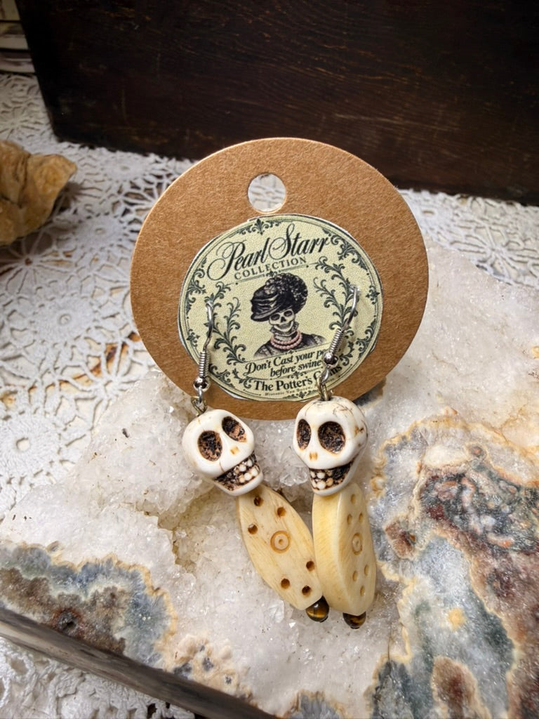 Pearl Starr skull earrings with cream-colored elongated bone beads decorated with brown dots and circles.