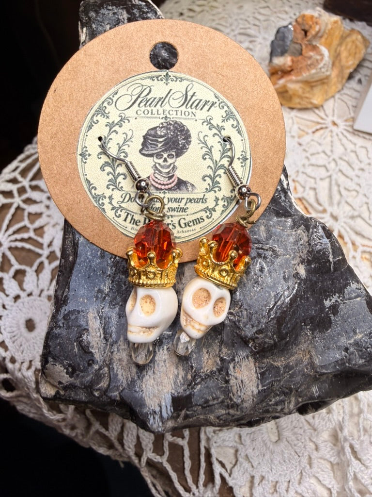 Pearl Starr earrings with ivory-colored skull beads, gold-colored crowns, amber-colored beads, and clear drops.