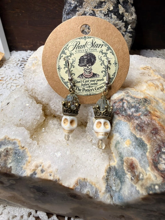 Pearl Starr ivory-colored skull earrings with antique brass-colored crowns, smoky gray faceted beads, and clear drops.