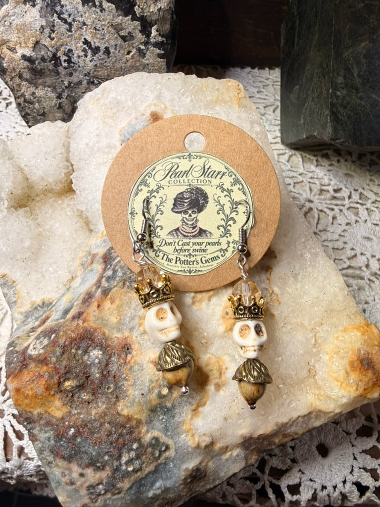 Pearl Starr earrings featuring crowned ivory-colored skulls, champagne-colored faceted beads, and brown acorn-shaped drops.